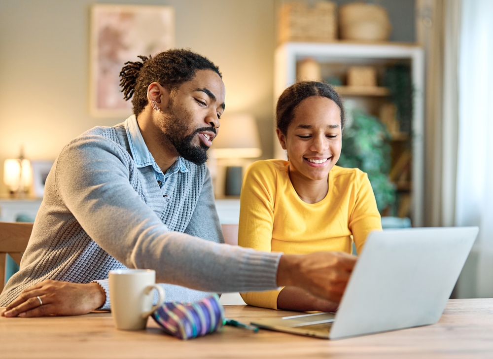 Dad teaching daughter something on her laptop.