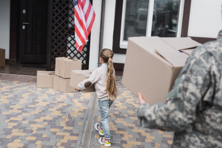 Military member and child carrying moving boxes.