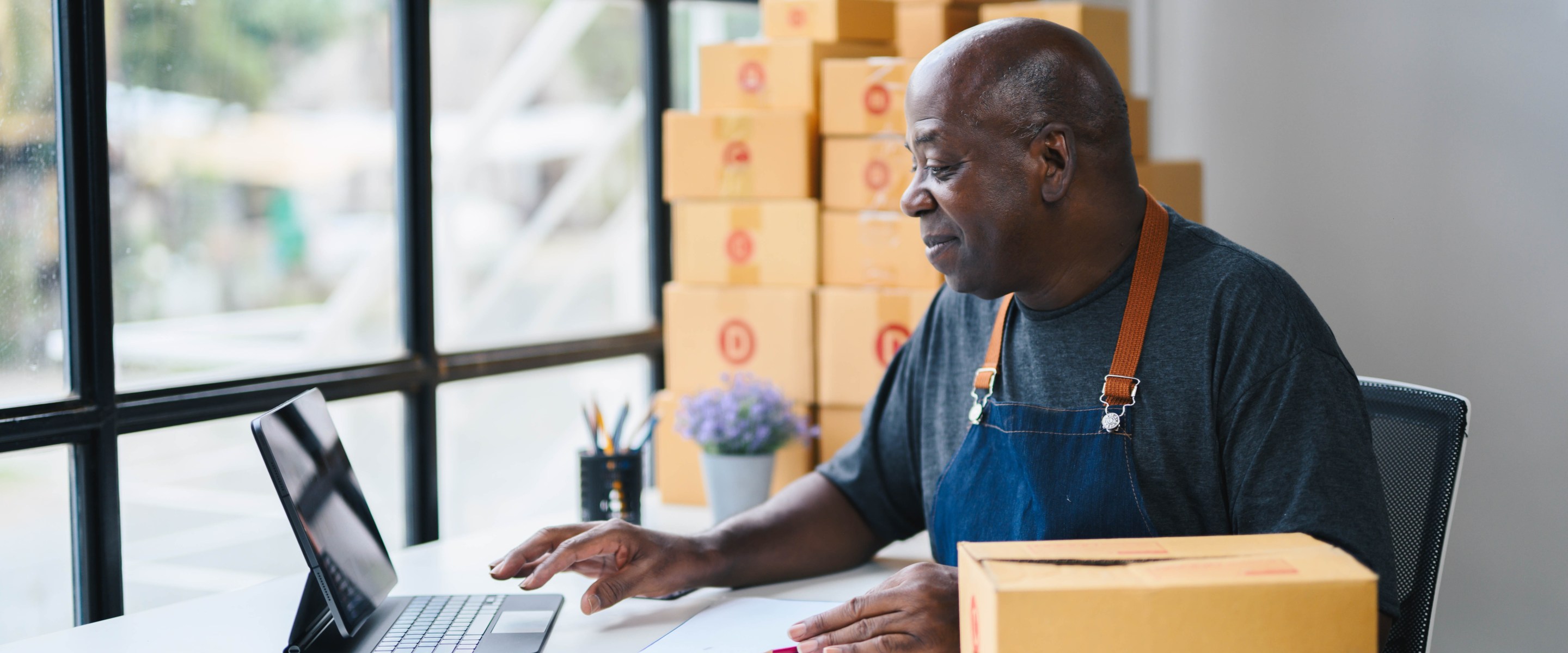 Black business owner working in front of laptop and packing boxes.