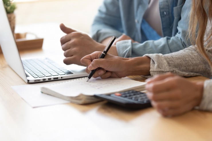 Close up of couple having a discussion with calculator, notebook, and laptop in front of them.