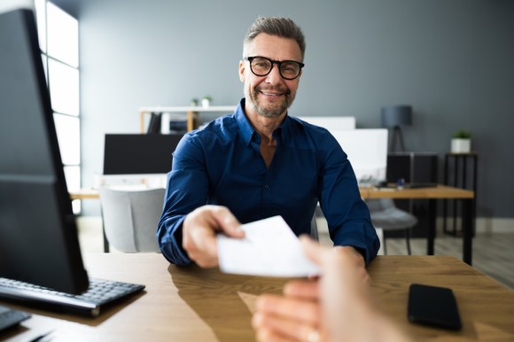 Middle-aged business man handing someone a paycheck.