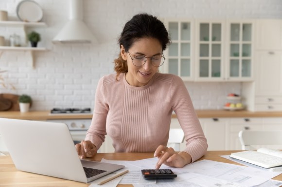 Woman sitting at the kitchen table with documents and a calculator in front of her.