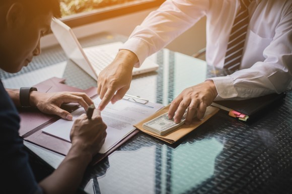 Man withdrawing a large sum of money from an account and signing paperwork.