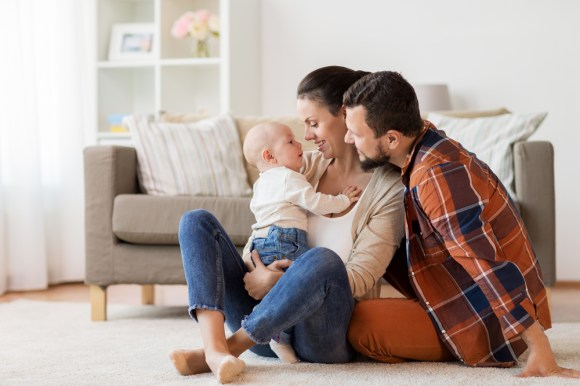 Young caucasian family with a baby sitting on the living room floor.