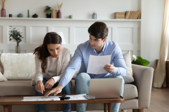 Concentrated, attentive millennial spouses sitting on a couch at home discussing finances.