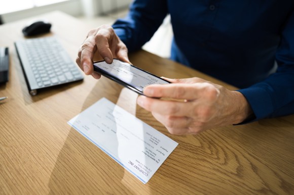 Close-up of a man taking a picture of a paper check to upload to the bank.