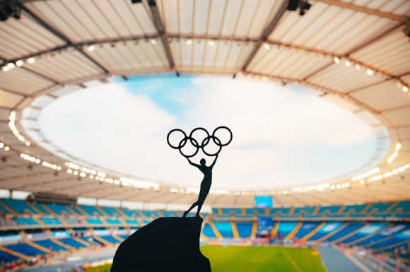 Silhouette of an Olympics statue in front of a sports arena.