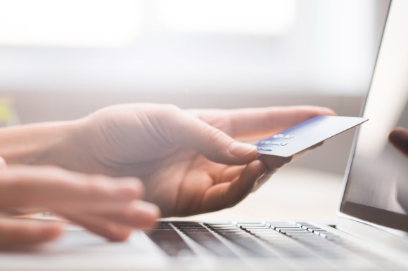 Hands holding a credit card, typing on a laptop's keyboard, shot close up.