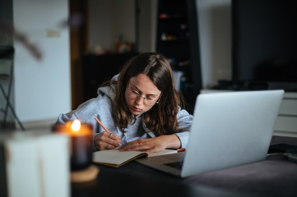 Woman writing in a notebook with her laptop open.