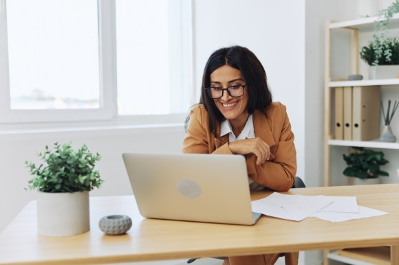 Businesswoman sitting at a desk working on her laptop with documents next to her.