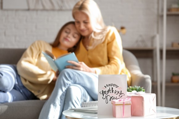 Woman cuddling with daughter on couch while opening Mother’s Day gifts.