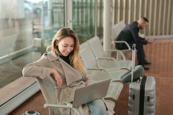 Woman working on her laptop with a suitcase next to her.
