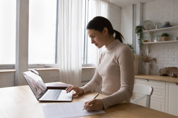 Self-employed business woman filling out a document and reading on her laptop.
