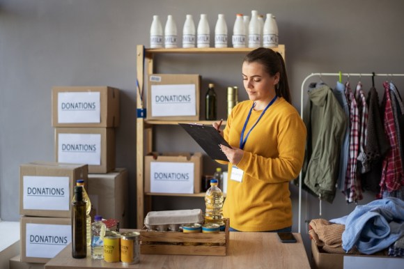 Woman running a charitable organization with supplies behind her as she writes on a clipboard.
