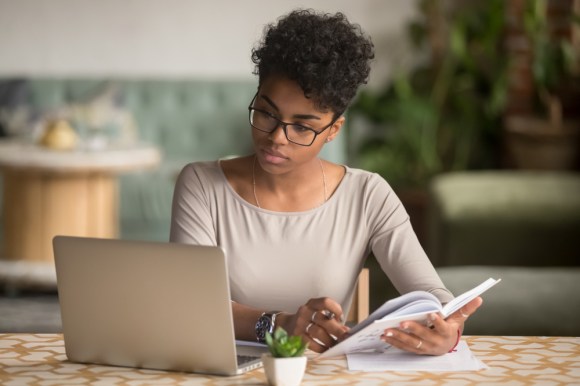 Young Black woman doing research and writing in notebook.
